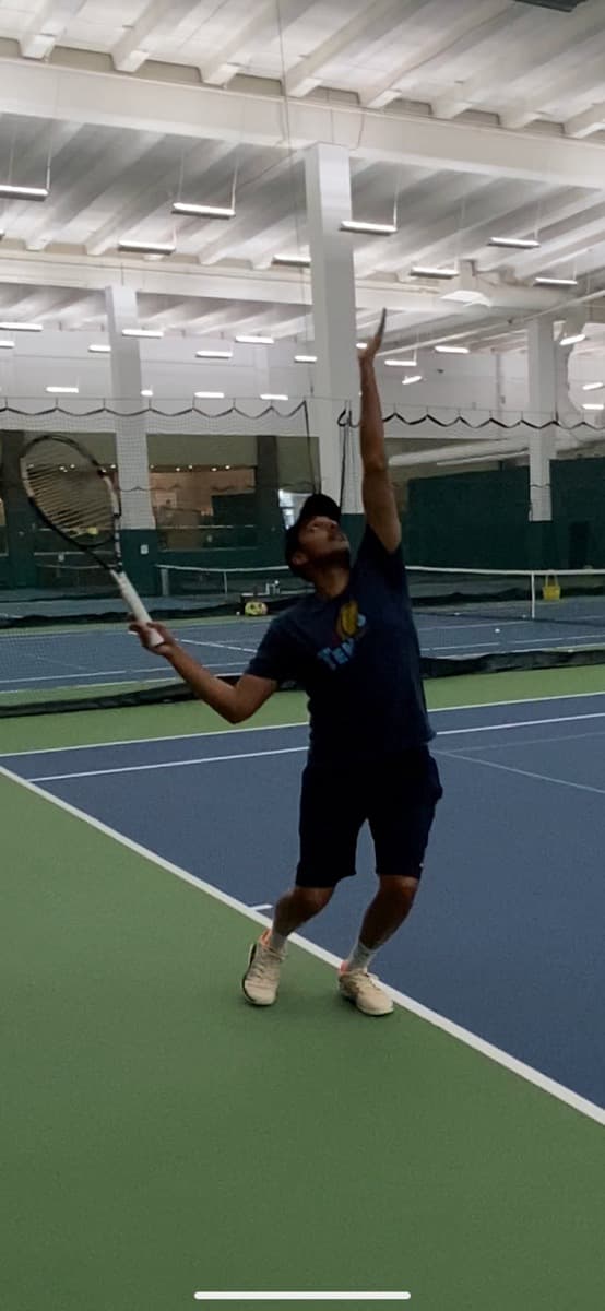 Kartik tossing a serve on an indoor court